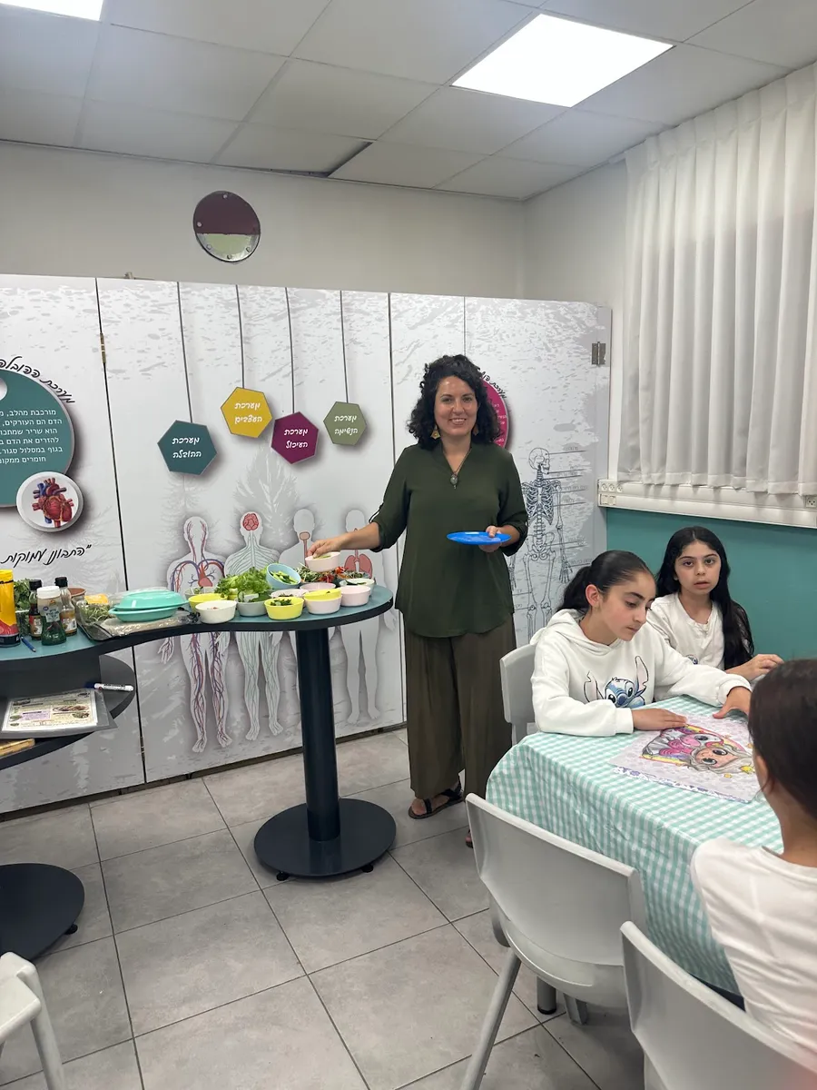 מיכל מובילה סדנה מול ילדים ועמדות עבודה