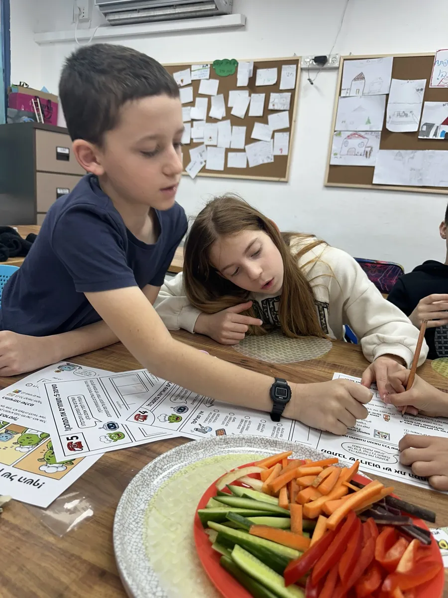 תלמידים פותרים דף משימה של השף הירוק ליד צלחת ירקות